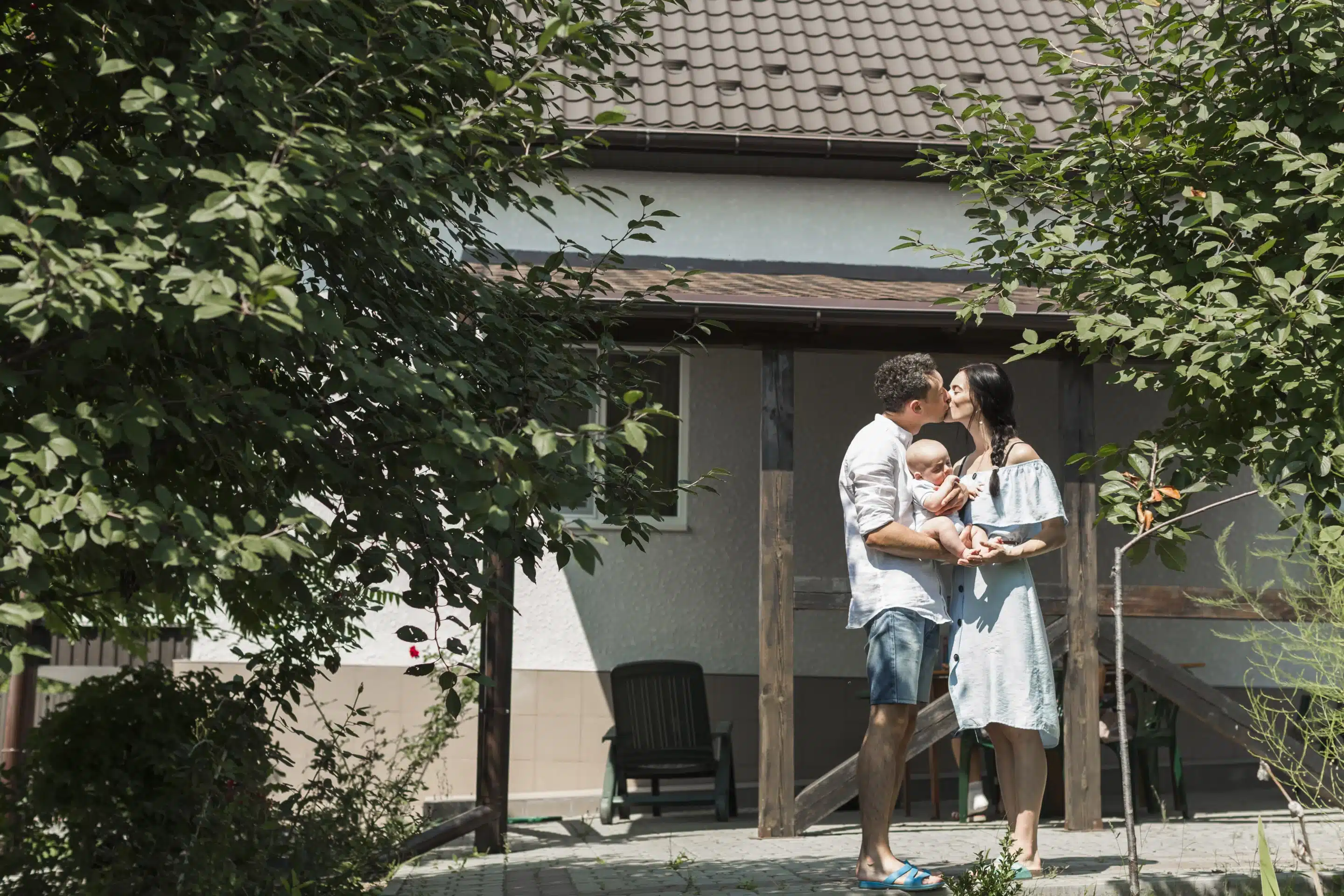 couple-carrying-their-baby-kissing-front-home